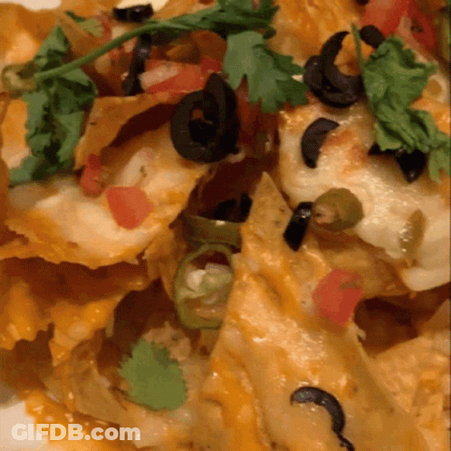 A Close Up Of A Plate Of Nachos With Black Olives And Tomatoes GIF