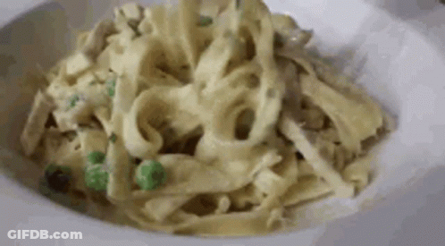 A Close Up Of A Plate Of Pasta With Peas And Chicken In A Sauce . GIF