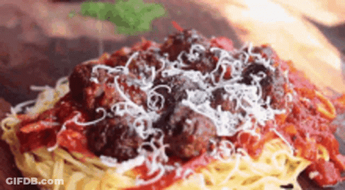 A Close Up Of A Plate Of Spaghetti And Meatballs With Sauce And Cheese On A Wooden Table . GIF