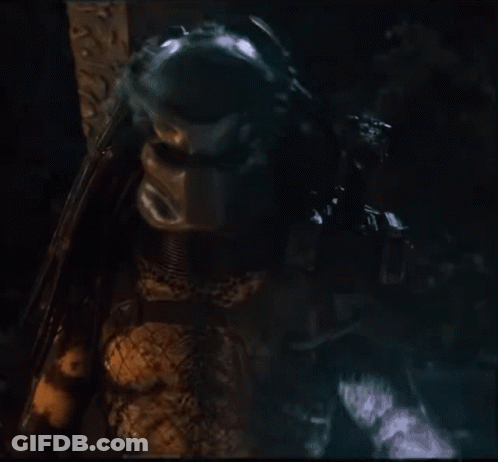 A Close Up Of A Predator Holding A Gun In A Dark Room GIF