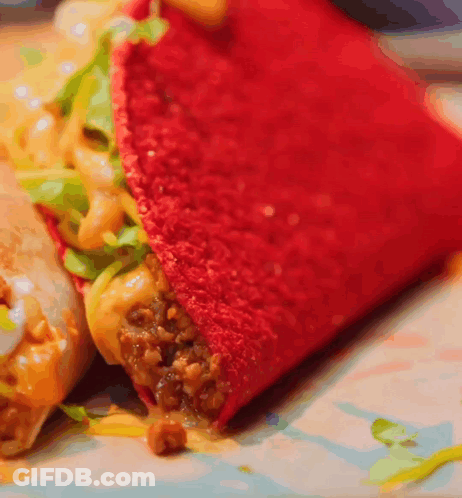 A Close Up Of A Red Taco With Meat And Cheese On A Plate GIF