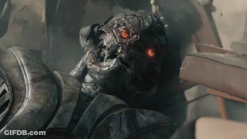 A Close Up Of A Robot With Red Eyes And The Letter T On His Chest GIF