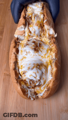 A Close Up Of A Sandwich With Cheese And Sauce On A Wooden Surface GIF