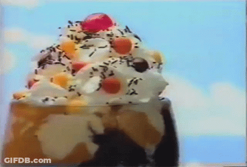 A Close Up Of A Sundae With Whipped Cream , Sprinkles , And A Cherry On Top . GIF