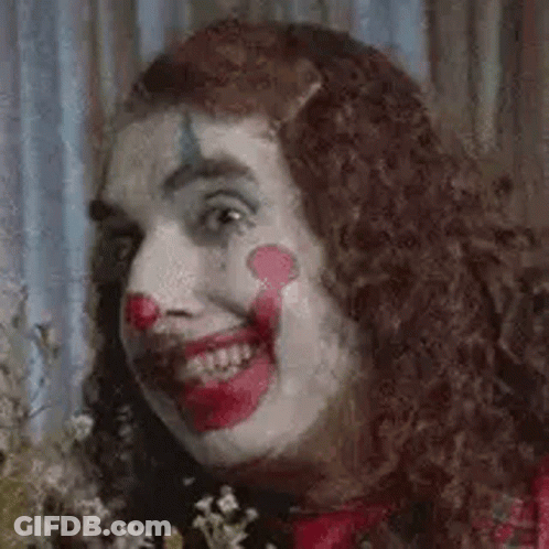 A Close Up Of A Woman Dressed As A Clown Holding Flowers . GIF