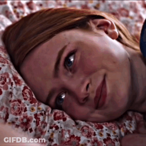 A Close Up Of A Woman Laying On A Bed With A Floral Comforter GIF
