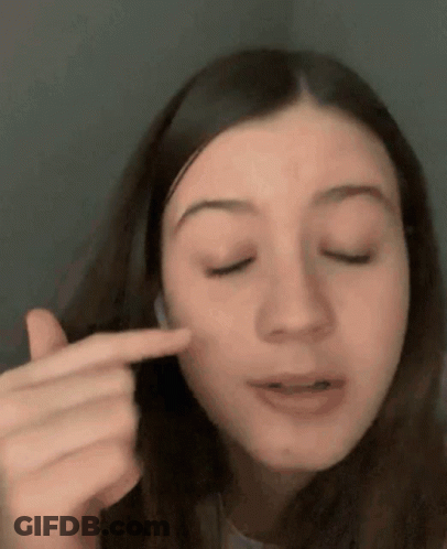 A Close Up Of A Woman Pointing At Her Face With Her Finger . GIF