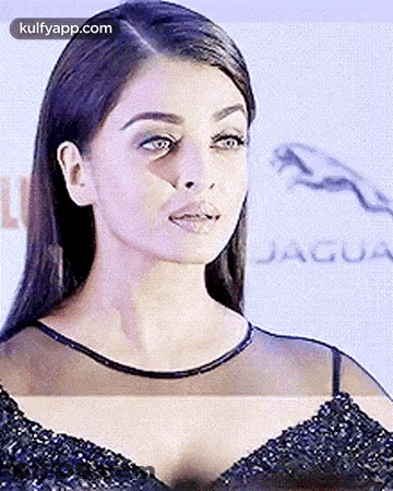 A Close Up Of A Woman 'S Face In A Black Dress With A Jaguar Logo In The Background . GIF
