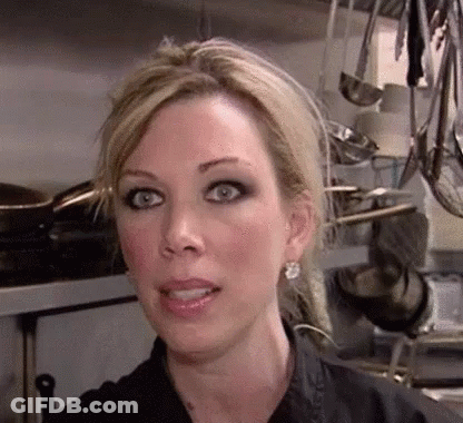 A Close Up Of A Woman 'S Face In A Kitchen With Pots And Pans Hanging From The Ceiling . GIF