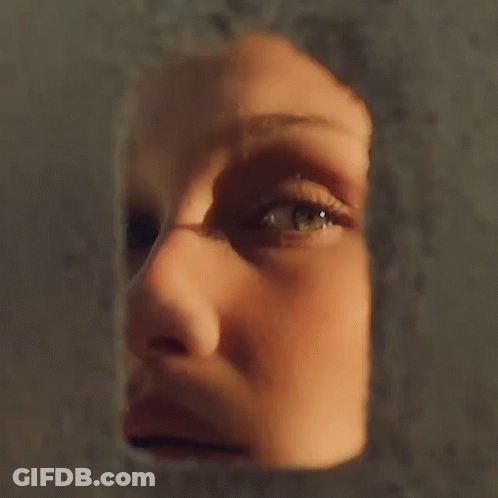 A Close Up Of A Woman 'S Face Looking Through A Hole In A Wall GIF