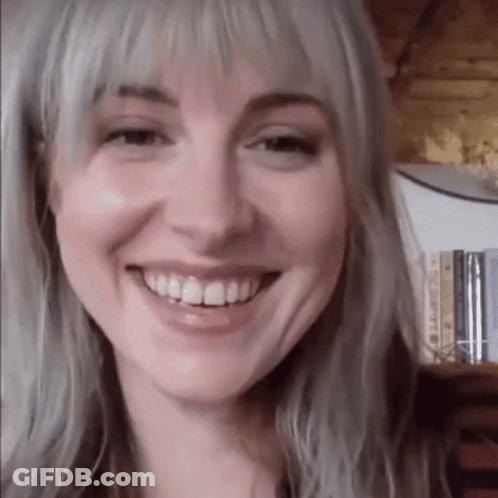 A Close Up Of A Woman 'S Face Smiling In Front Of A Bookshelf Filled With Books . GIF