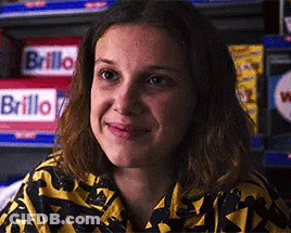 A Close Up Of A Woman 'S Face Smiling In Front Of A Shelf . GIF