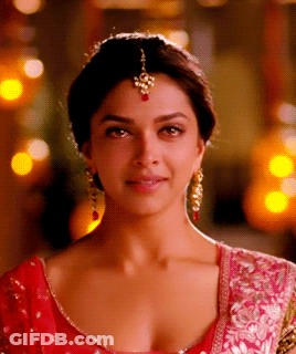 A Close Up Of A Woman 'S Face Wearing A Red Top And Gold Earrings GIF