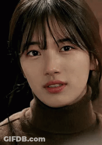 A Close Up Of A Woman 'S Face Wearing A Turtleneck Sweater And Looking At The Camera . GIF
