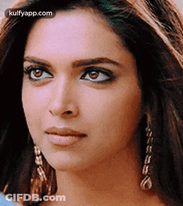 A Close Up Of A Woman 'S Face Wearing Earrings And A Blue Shirt . GIF