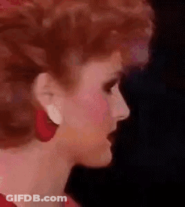 A Close Up Of A Woman 'S Face Wearing Red Earrings And Red Hair . GIF