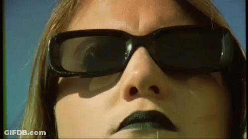 A Close Up Of A Woman 'S Face Wearing Sunglasses And Black Lipstick . GIF