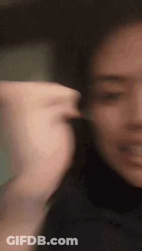 A Close Up Of A Woman 'S Face With A Blurry Background And A Hand Behind Her Ear . GIF