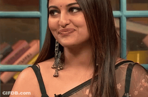 A Close Up Of A Woman 'S Face With A Bookshelf In The Background GIF