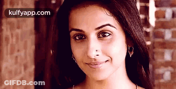 A Close Up Of A Woman 'S Face With A Brick Wall In The Background And Kulfyapp.com In The Corner GIF