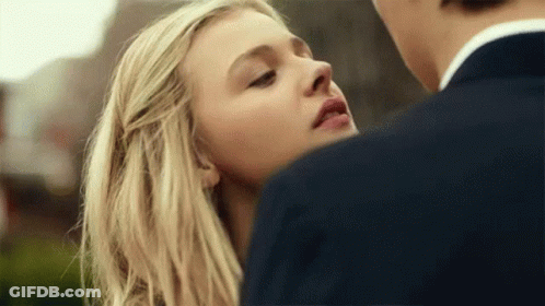 A Close Up Of A Woman 'S Face With A Man In A Suit Behind Her . GIF