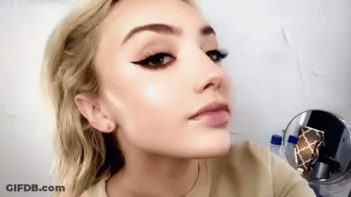 A Close Up Of A Woman 'S Face With A Mirror Behind Her . GIF