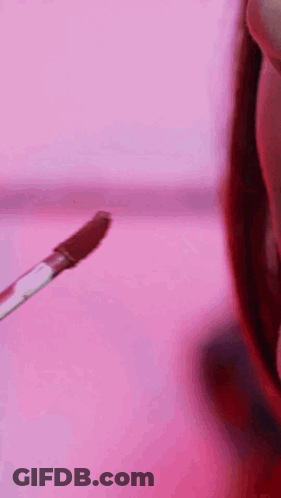A Close Up Of A Woman 'S Face With A Pink Background And Lipstick On Her Lips . GIF