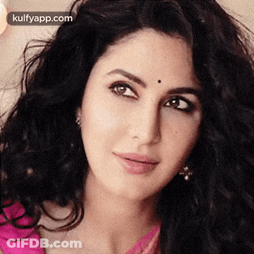 A Close Up Of A Woman 'S Face With A Pink Shirt And Earrings . GIF