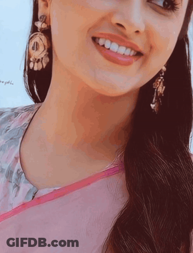 A Close Up Of A Woman 'S Face With A Pink Shirt And Earrings GIF