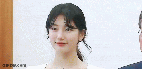 A Close Up Of A Woman 'S Face With A Ponytail And A Man In A Suit Behind Her . GIF