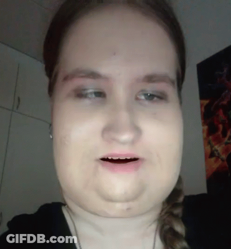 A Close Up Of A Woman 'S Face With A Poster On The Wall Behind Her GIF