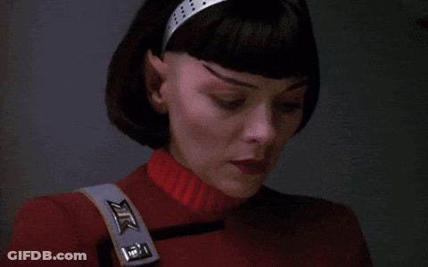 A Close Up Of A Woman 'S Face With A Red Sweater And A Strap That Says Xtc On It GIF