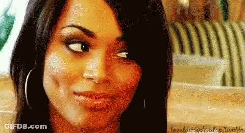 A Close Up Of A Woman 'S Face With A Smile On Her Face And A Striped Chair In The Background . GIF
