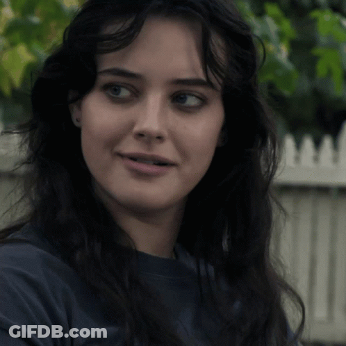 A Close Up Of A Woman 'S Face With A White Picket Fence Behind Her GIF