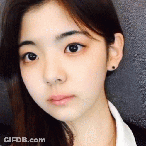 A Close Up Of A Woman 'S Face With A White Shirt And Black Earrings GIF