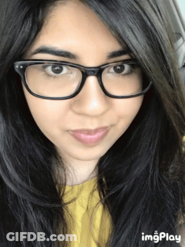 A Close Up Of A Woman 'S Face With A Yellow Shirt And Glasses GIF