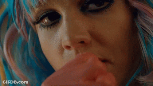 A Close Up Of A Woman 'S Face With Blue And Pink Hair Holding A Red Object . GIF