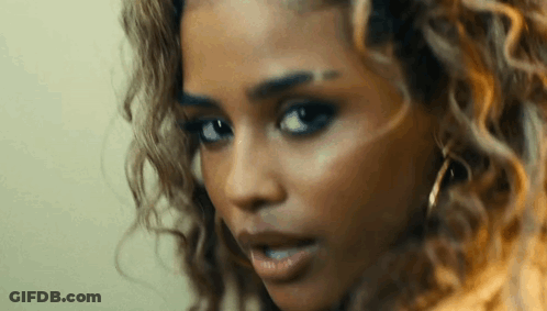 A Close Up Of A Woman 'S Face With Curly Hair And Earrings Looking At The Camera . GIF