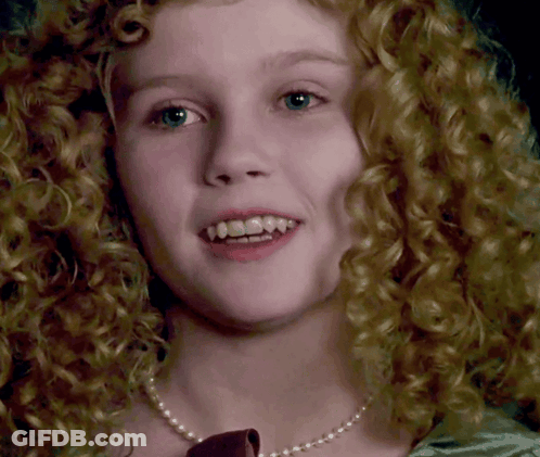 A Close Up Of A Woman 'S Face With Curly Hair Wearing A Pearl Necklace GIF