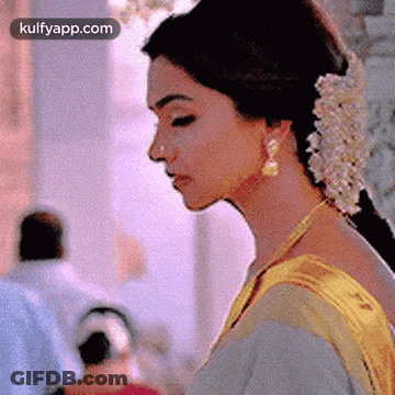 A Close Up Of A Woman 'S Face With Flowers In Her Hair And Earrings . GIF