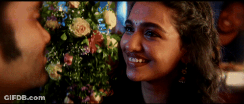 A Close Up Of A Woman 'S Face With Flowers In The Background GIF