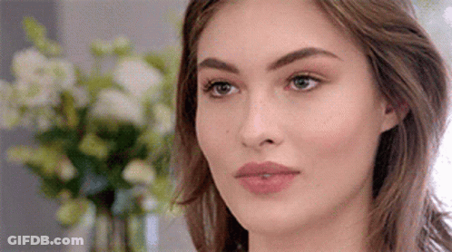 A Close Up Of A Woman 'S Face With Flowers In The Background . GIF