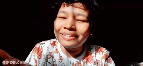 A Close Up Of A Woman 'S Face With Her Eyes Closed And A Floral Shirt . GIF