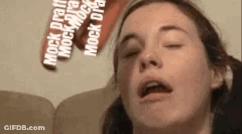 A Close Up Of A Woman 'S Face With Her Eyes Closed And A Sign Behind Her That Says `` Mock Draft '' . GIF