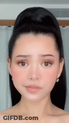 A Close Up Of A Woman 'S Face With Her Hair In A Bun And Earrings . GIF