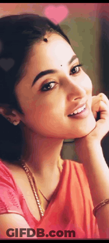 A Close Up Of A Woman 'S Face With Her Hand On Her Chin . She Is Wearing A Red Saree And Smiling . GIF
