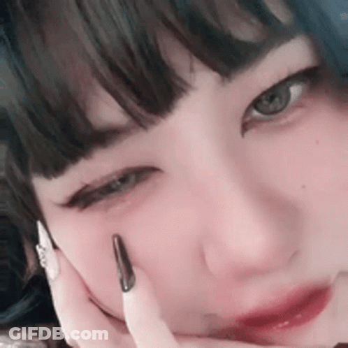 A Close Up Of A Woman 'S Face With Her Hand On Her Face And A Black Nail . GIF