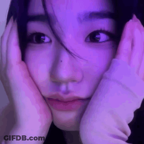 A Close Up Of A Woman 'S Face With Her Hands On Her Face In Front Of A Purple Light . GIF