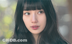 A Close Up Of A Woman 'S Face With Long Black Hair And Bangs Looking At The Camera . GIF