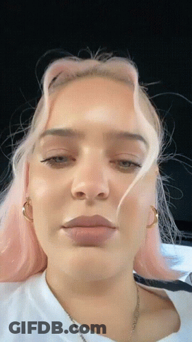 A Close Up Of A Woman 'S Face With Pink Hair And A White Shirt GIF